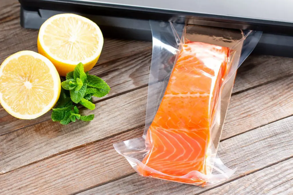 Vacuum-sealed fresh salmon with lemon and mint on wood surface.
