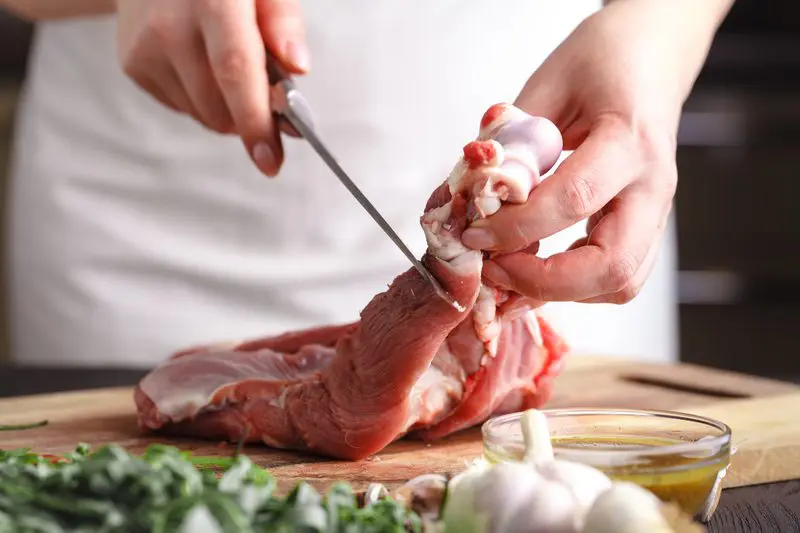 Female Chef cutting raw lamb meat on wooden board prepared for cooking